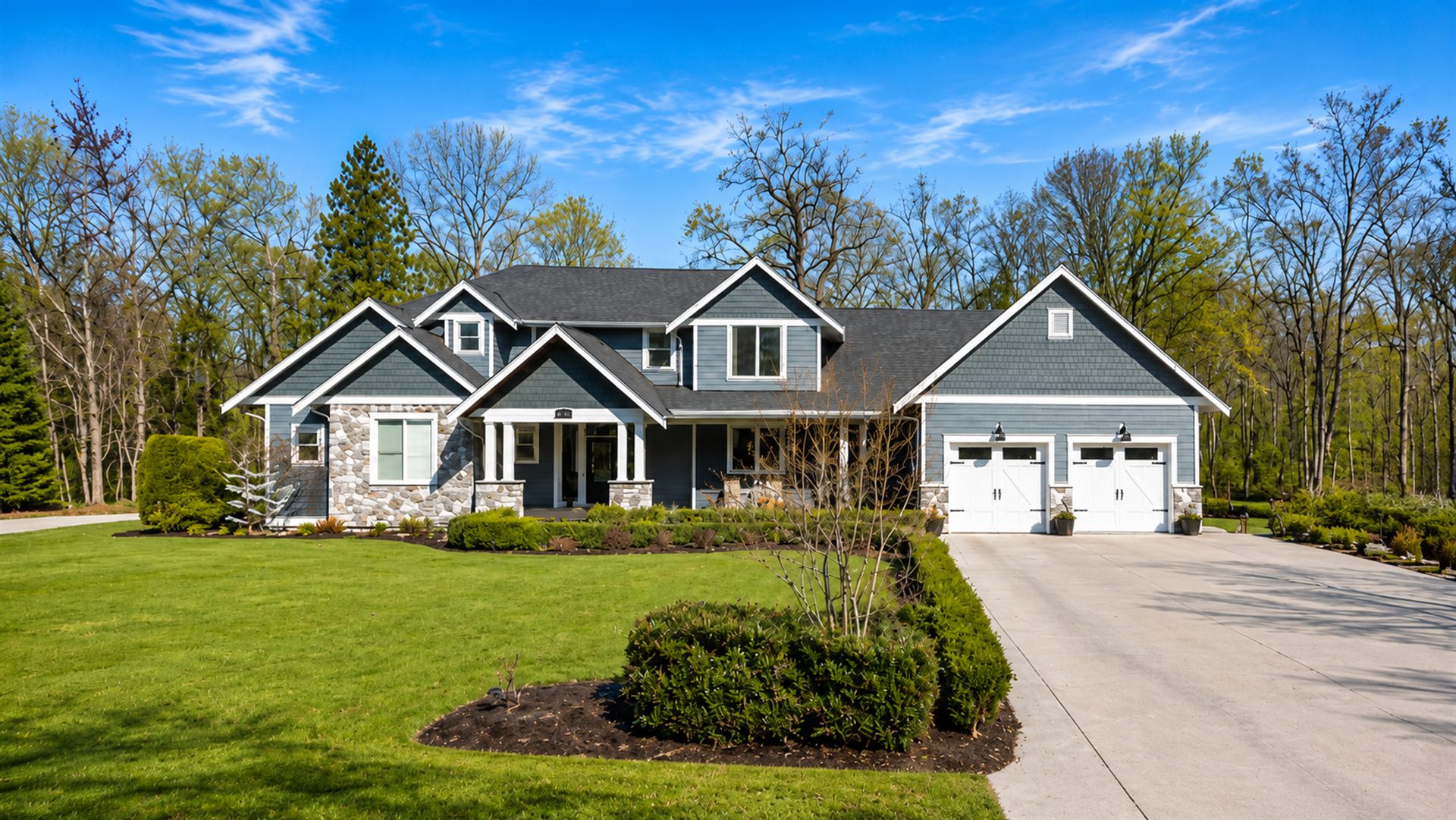 Two-storey blue-grey craftsman home with stone pillars and carriage garage doors